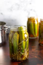 jars of pickled okra on a wooden counter with a marble backsplash