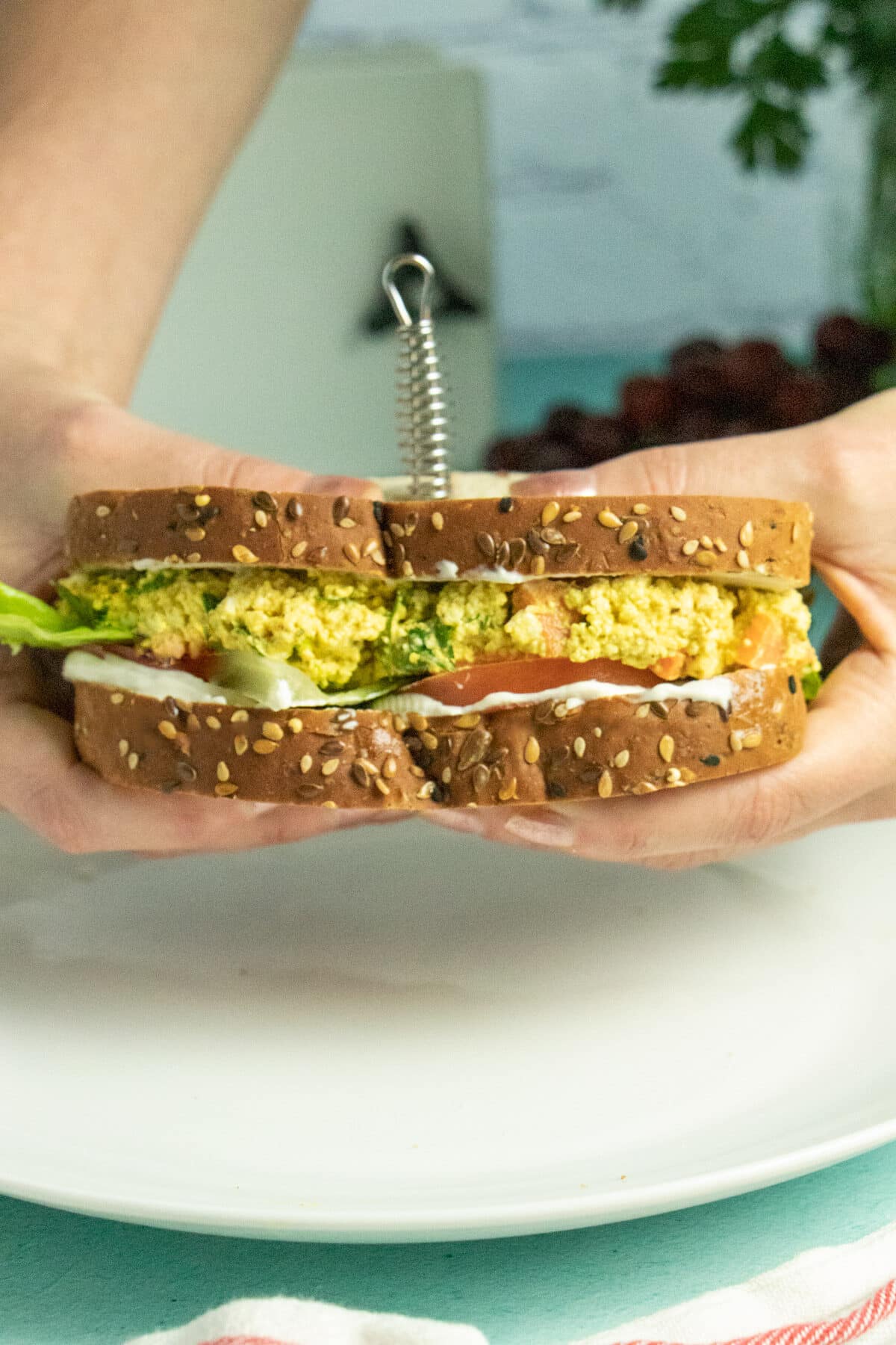 hands holding a tofu egg salad sandwich with lettuce and tomato