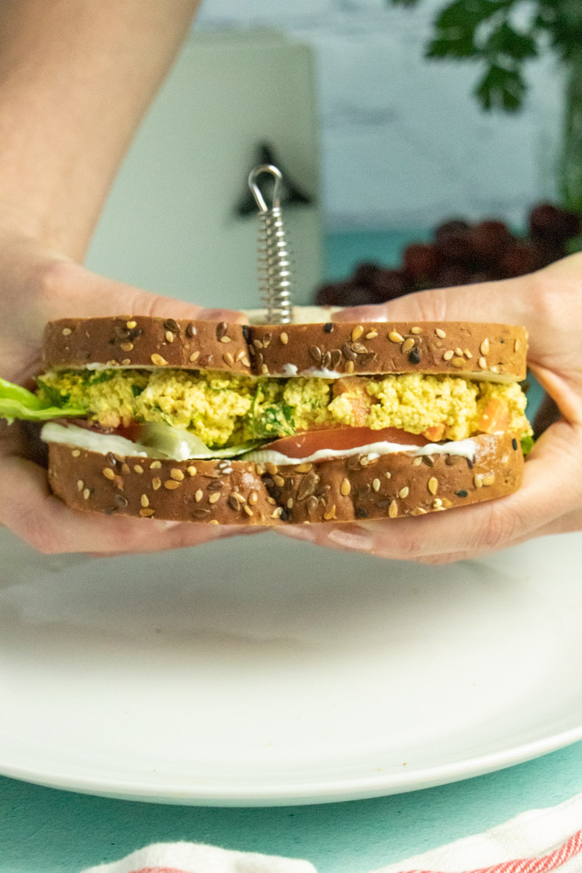hands holding a tofu egg salad sandwich with lettuce and tomato