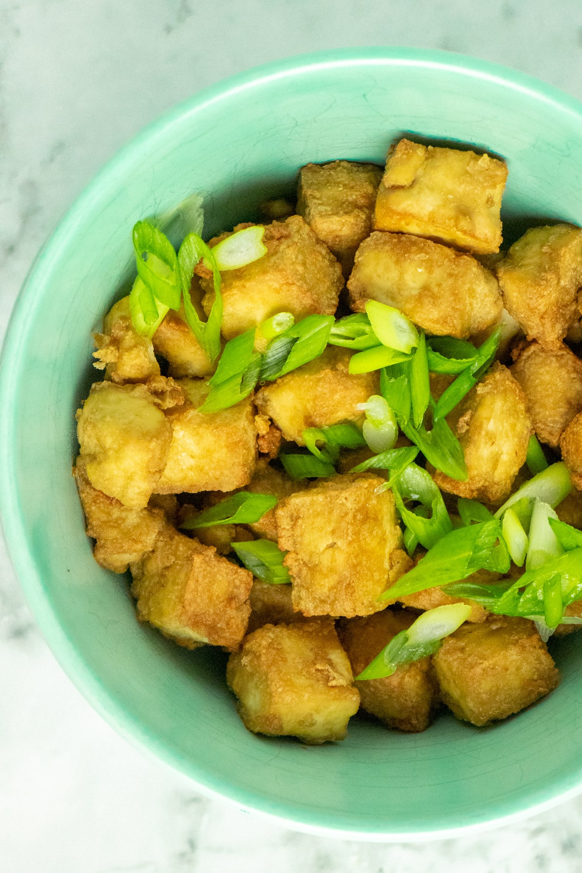overhead photo of air fryer tofu in a blue bowl with green onions sprinkled on top