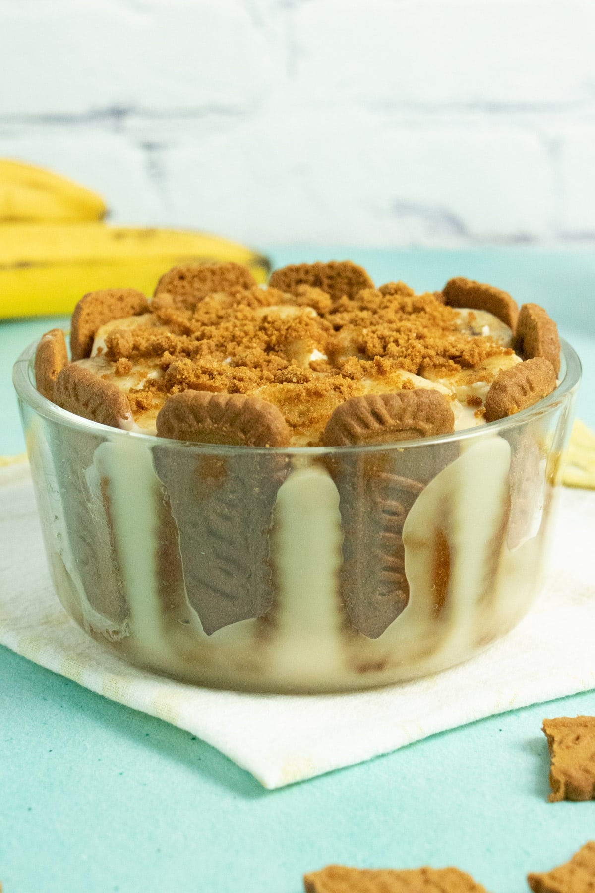 glass serving bowl of biscoff cookies standing in a bowl of vegan banana pudding with crumbled cookies on top