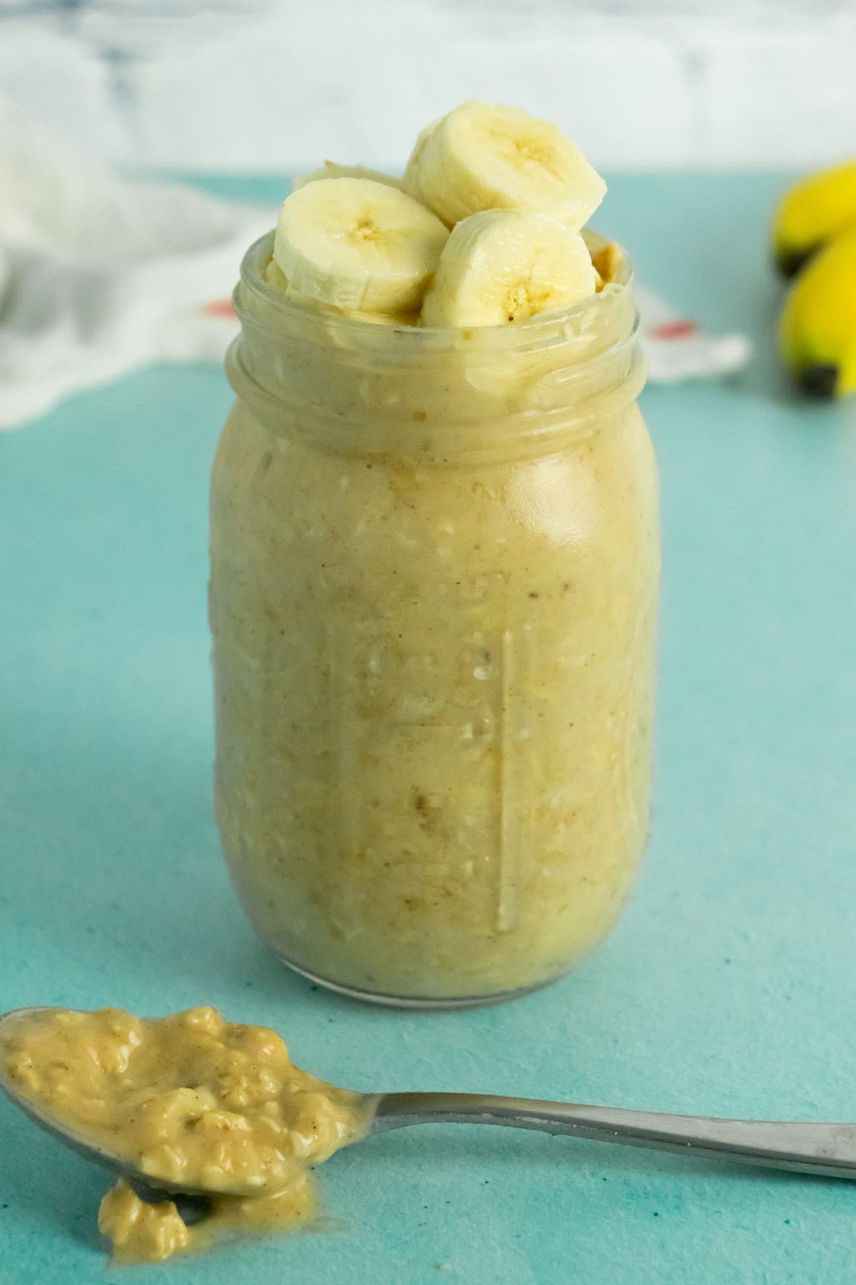 mason jar of peanut butter banana overnight oats with bananas and a tea towel in the background