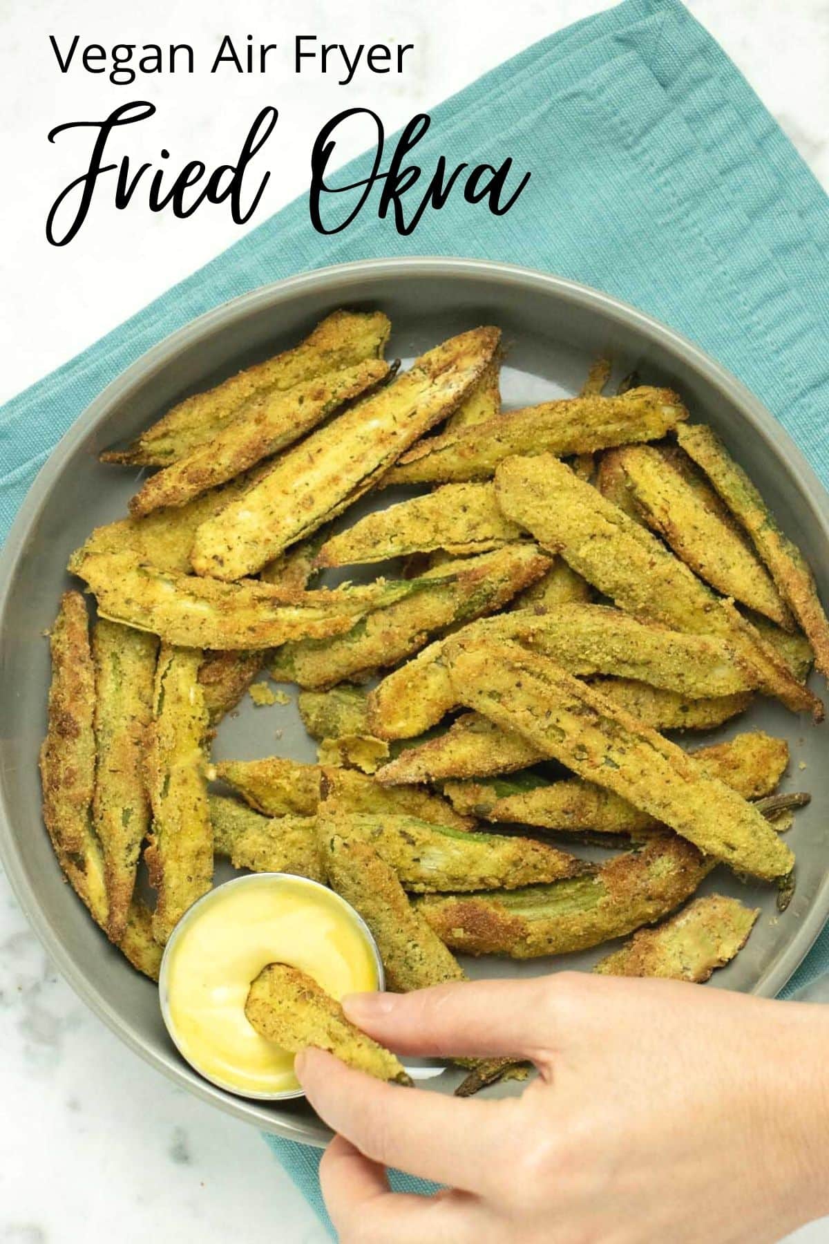 serving platter of air fryer okra, a hand is dipping a piece into a creamy sauce, text overlay