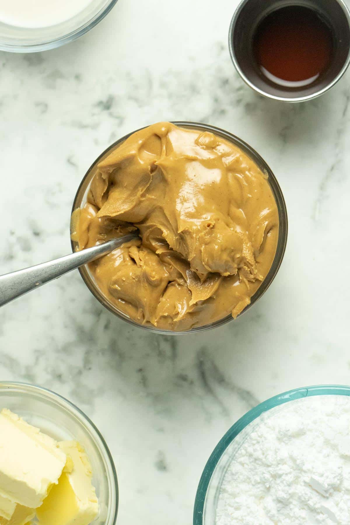 glass bowl of creamy peanut butter with frosting ingredients around it in bowls