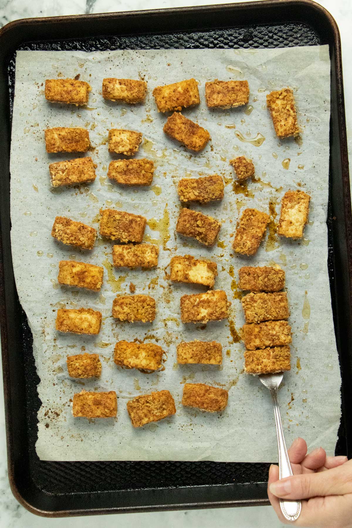 using a fork to scoop up pieces of crispy tofu from a baking sheet