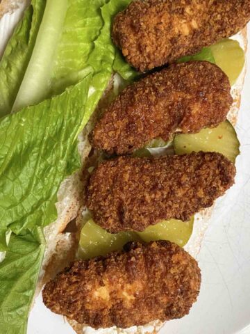 open hoagie roll with lettuce, pickles, mayo, and Gardein Nashville Hot Chickenless Tenders on it