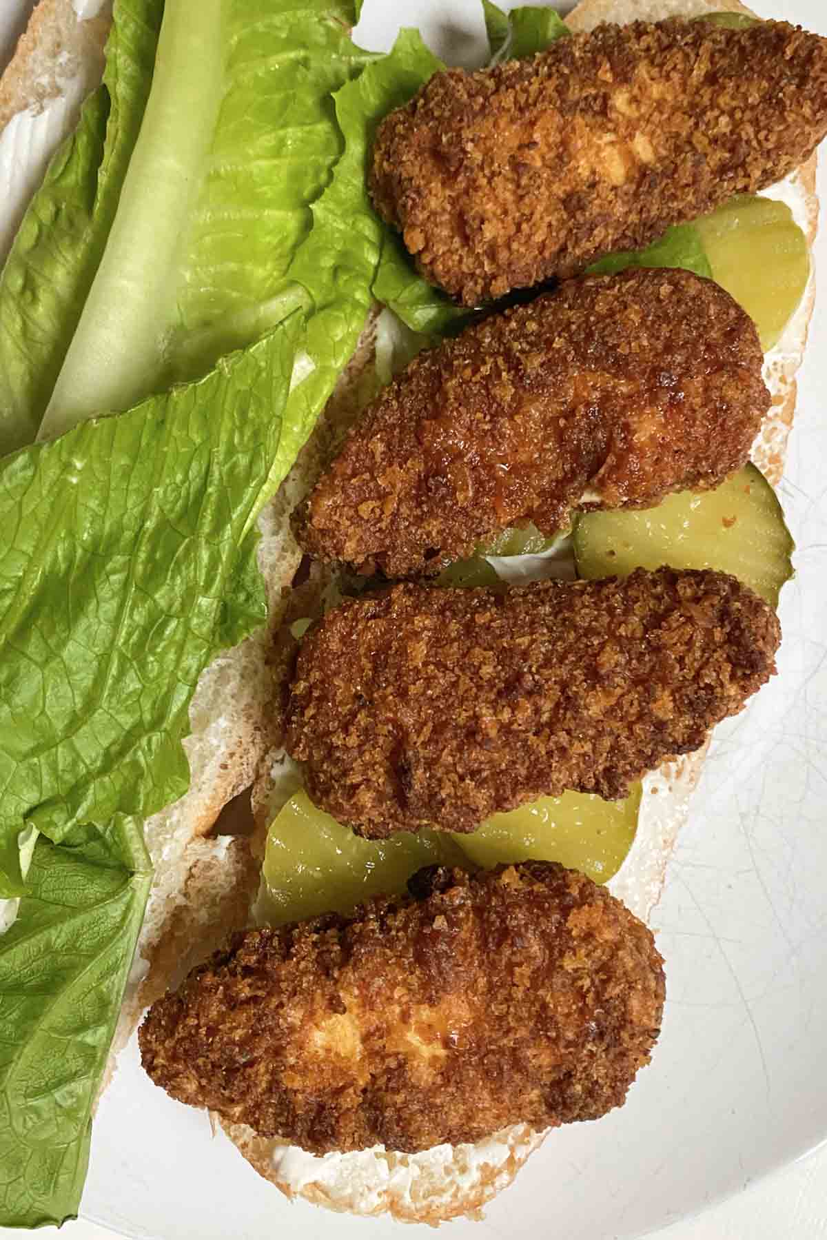 open hoagie roll with lettuce, pickles, mayo, and Gardein Nashville Hot Chickenless Tenders on it