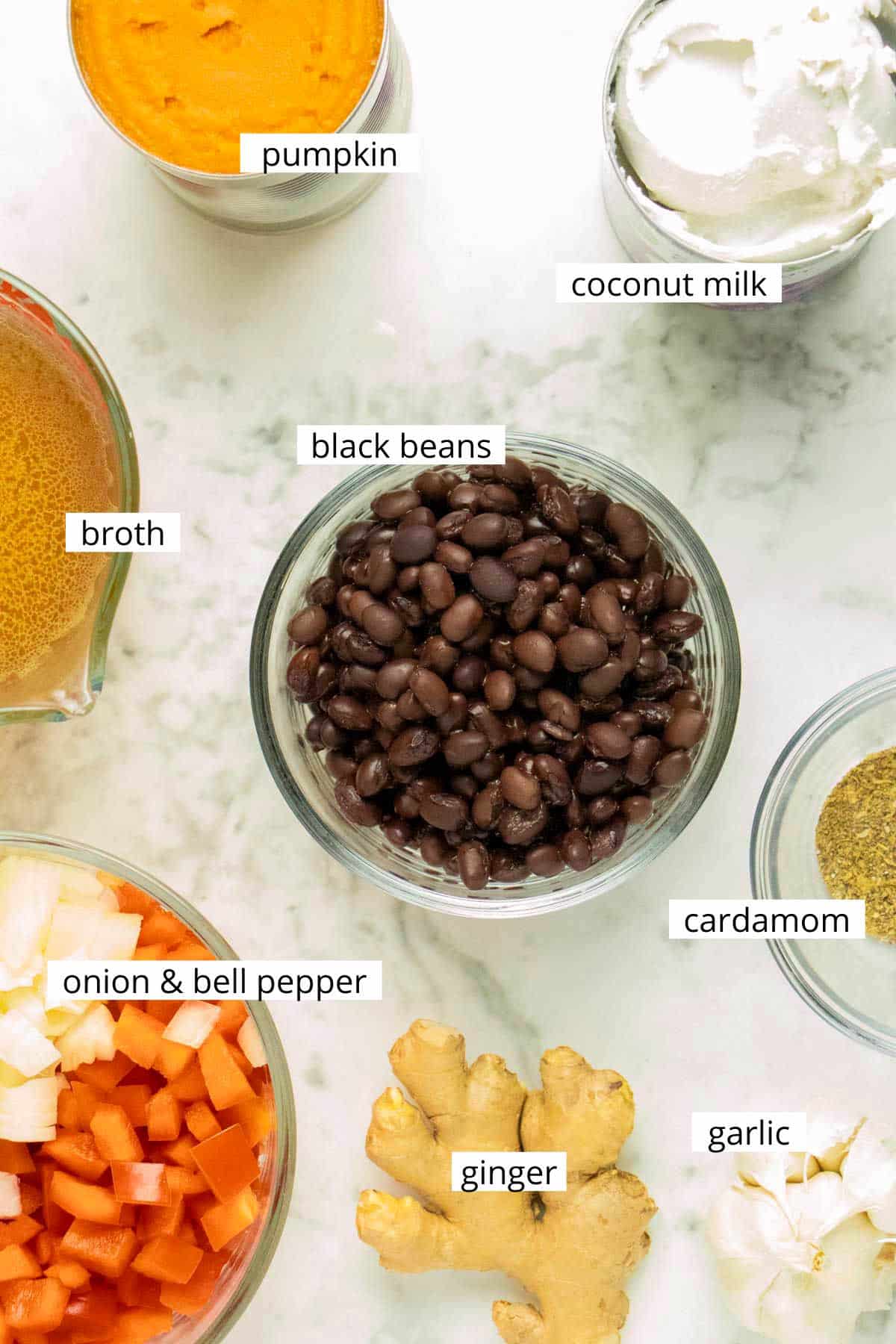 black beans, pumpkin, and other soup ingredients on a marble table with text labels on each one