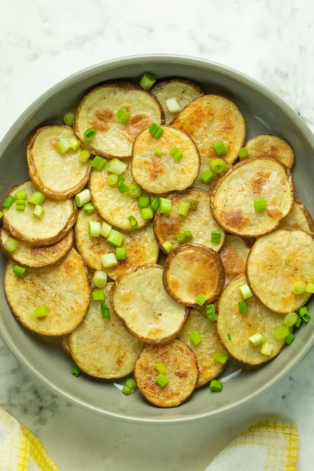 serving plate of crispy, baked sliced potatoes topped with chopped green onions