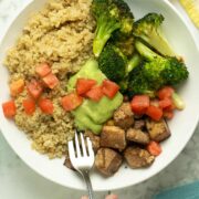quinoa bowl with roasted tofu and broccoli topped with pesto and tomatoes