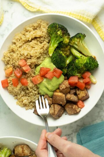 quinoa bowl with roasted tofu and broccoli topped with pesto and tomatoes