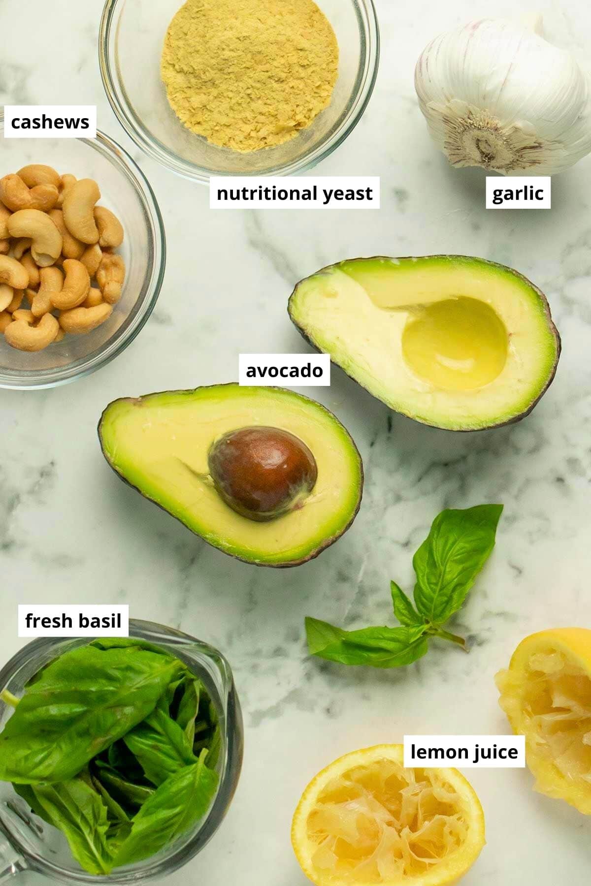 avocado, basil, and other vegan avocado pesto pasta ingredients in bowls on a marble table