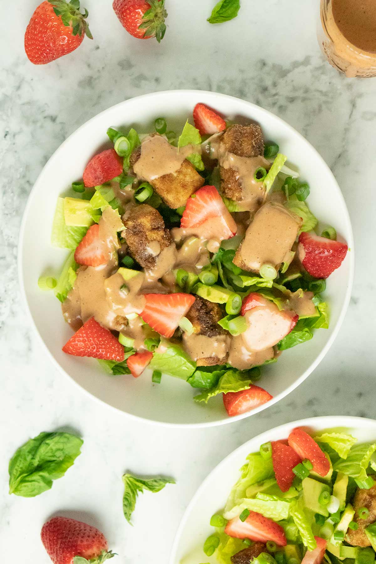 crispy tofu salad in a white bowl with romaine, strawberries, avocado, green onions, and creamy dressing