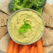 pesto hummus in a serving dish surrounded by pita points and vegetables