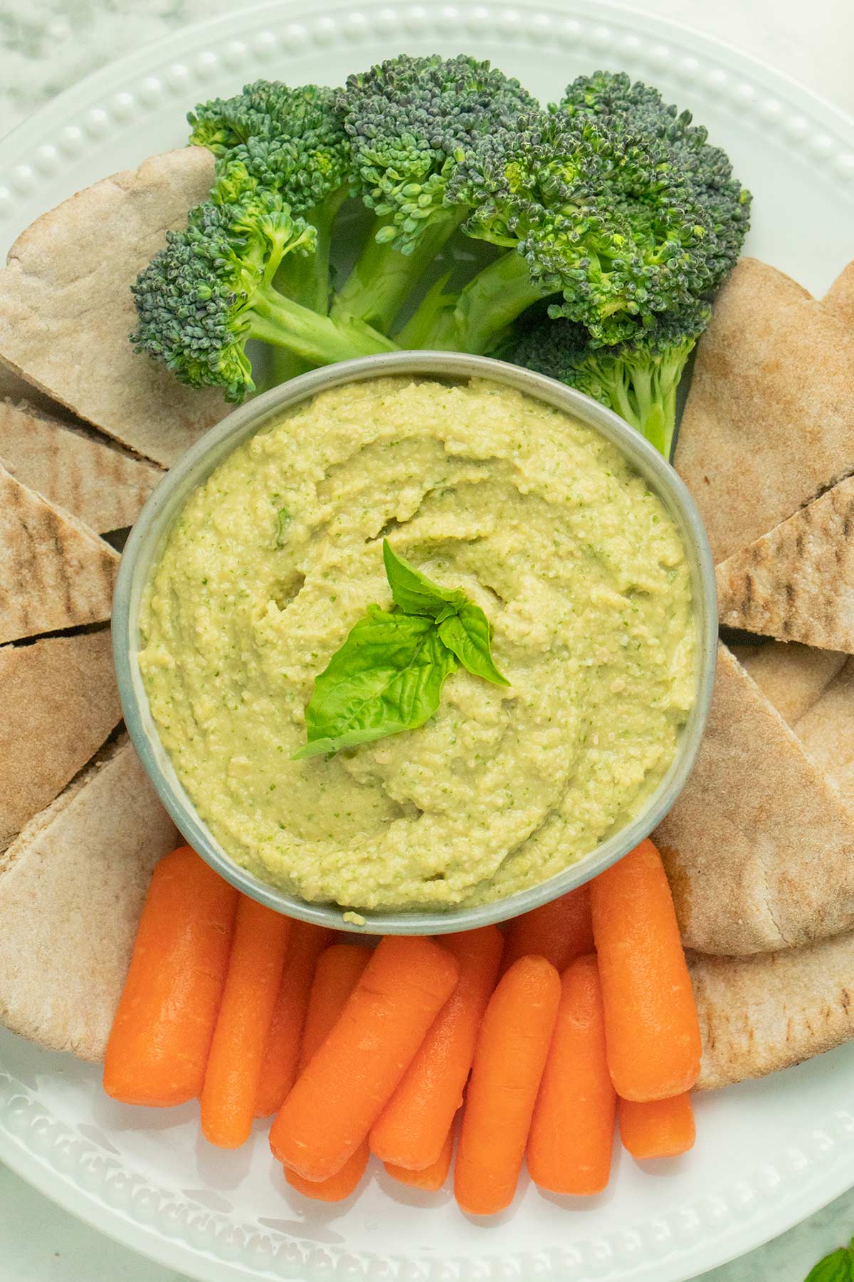 pesto hummus in a serving dish surrounded by pita points and vegetables
