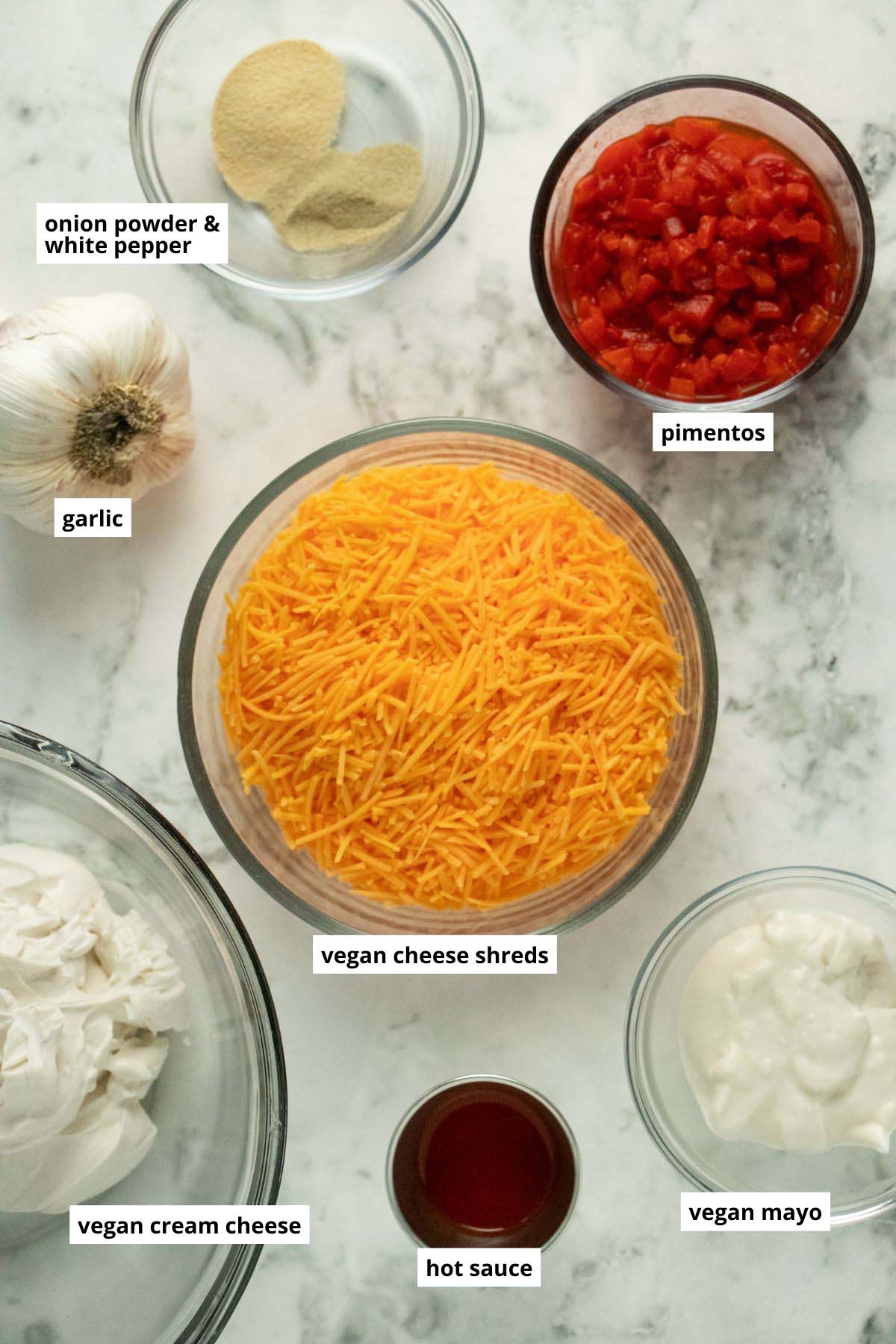vegan cheese, pimentos, and other pimento cheese ingredients in bowls on a white table