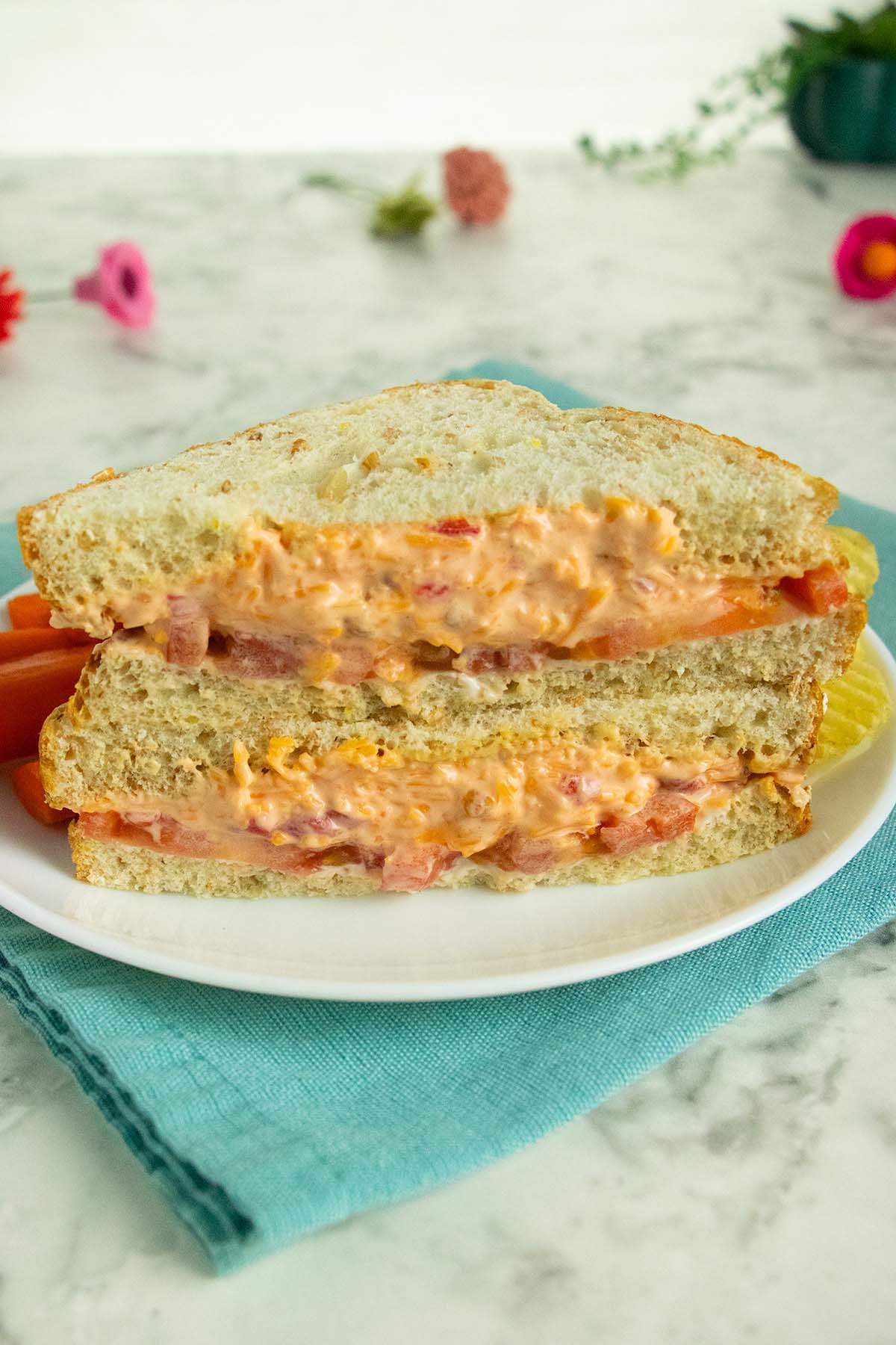 vegan tomato sandwich with pimento cheese on a white table with flowers in the background