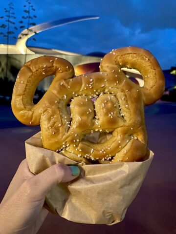 hand holding a Mickey Pretzel in front of Mission Space