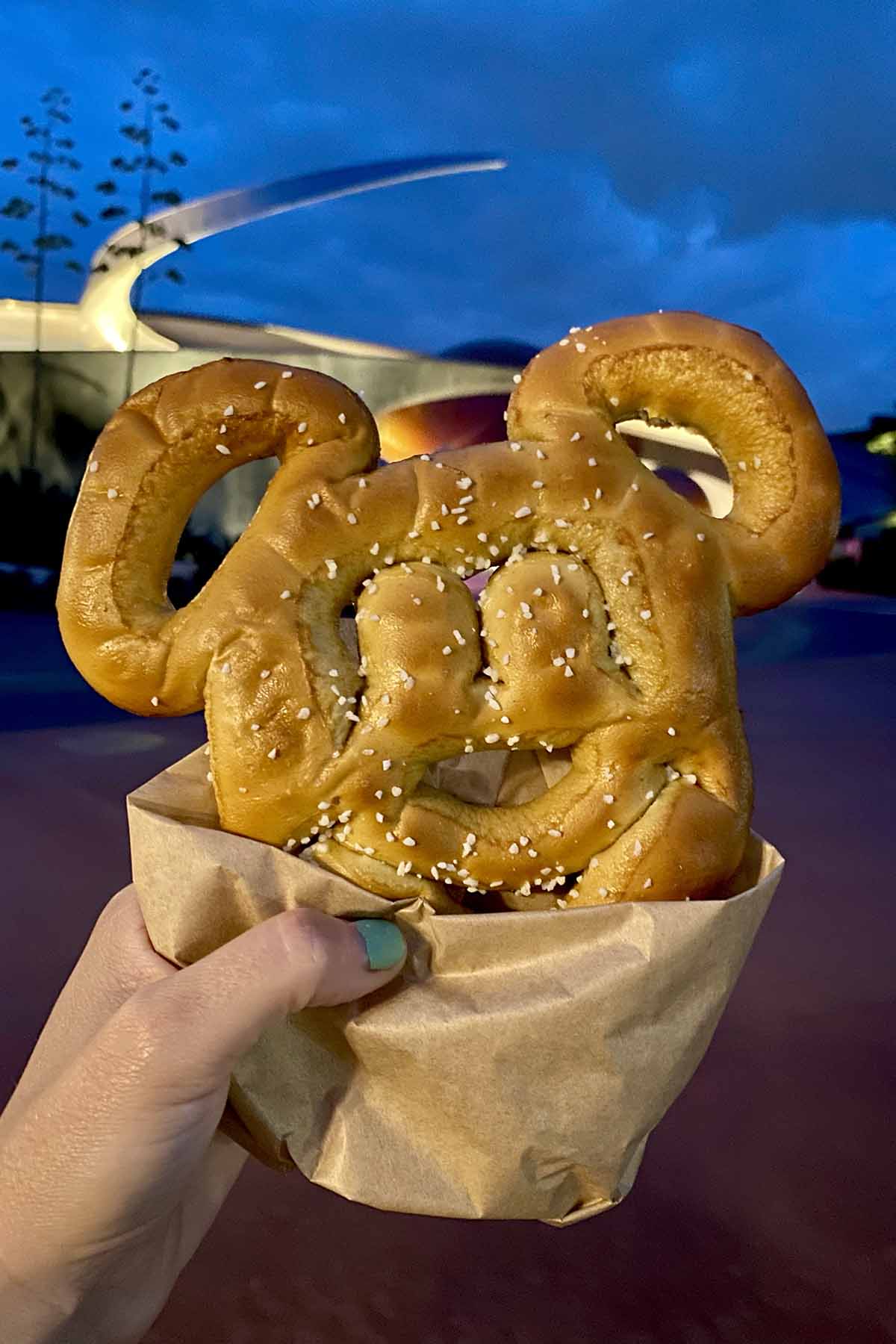 hand holding a Mickey Pretzel in front of Mission Space