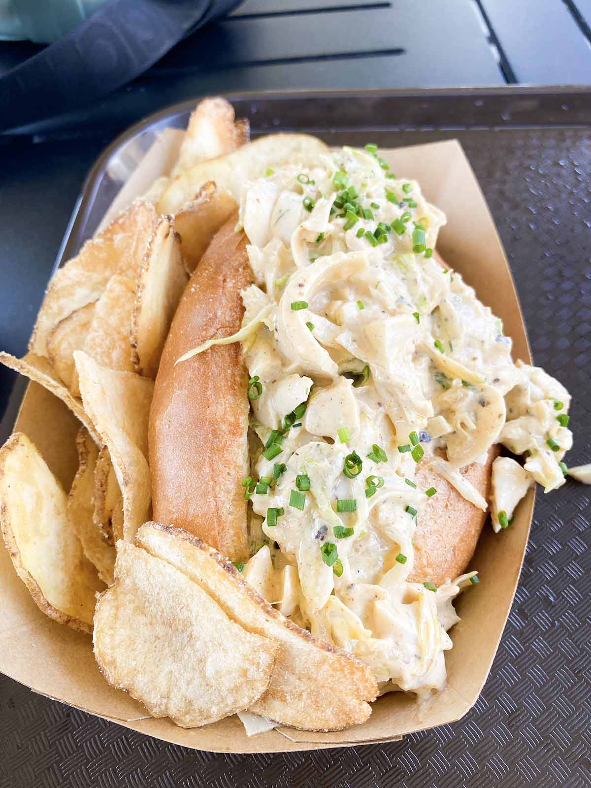 vegan lobster roll with chips in a paper tray