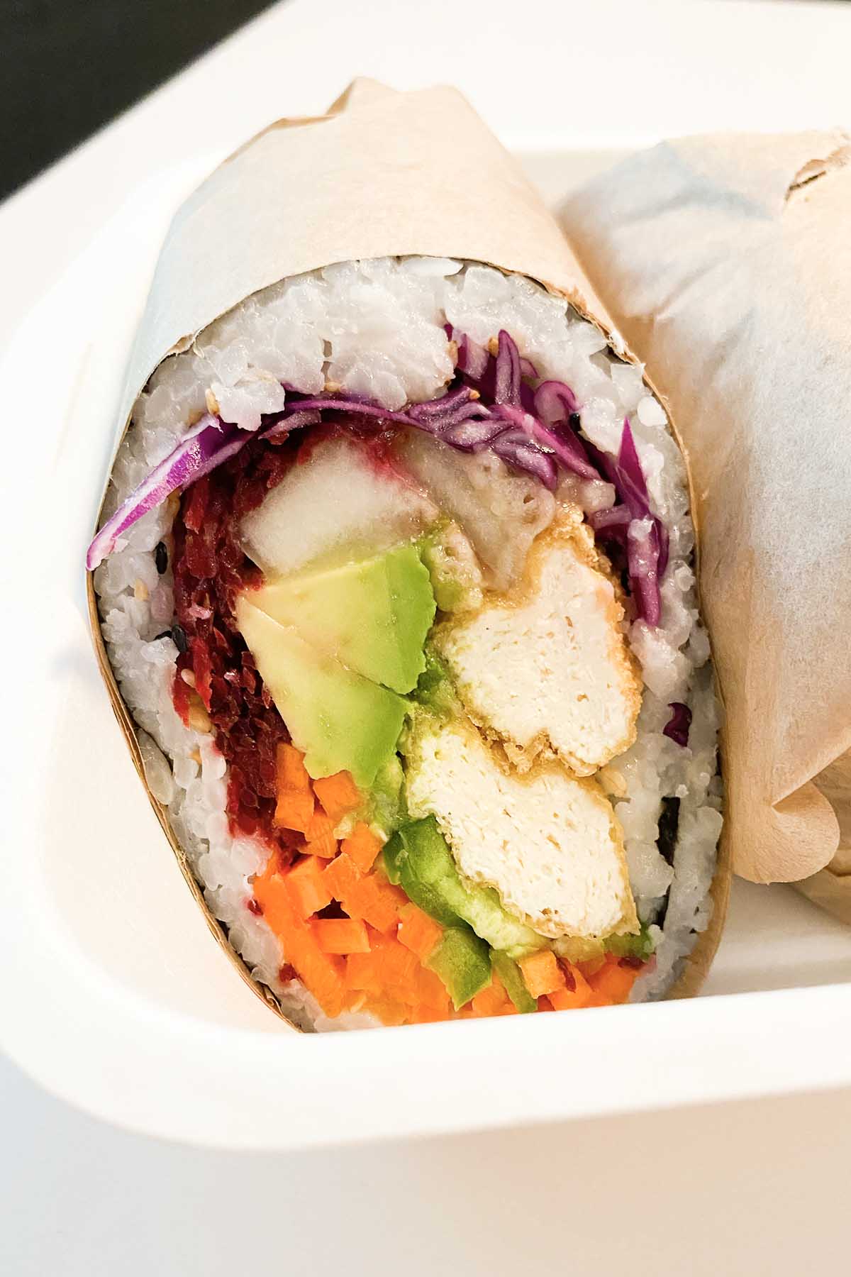 Poke Burri sushi burrito in paper wrapper with avocado, beets, carrots, pickles, cabbage, jalapeño, and crispy tofu