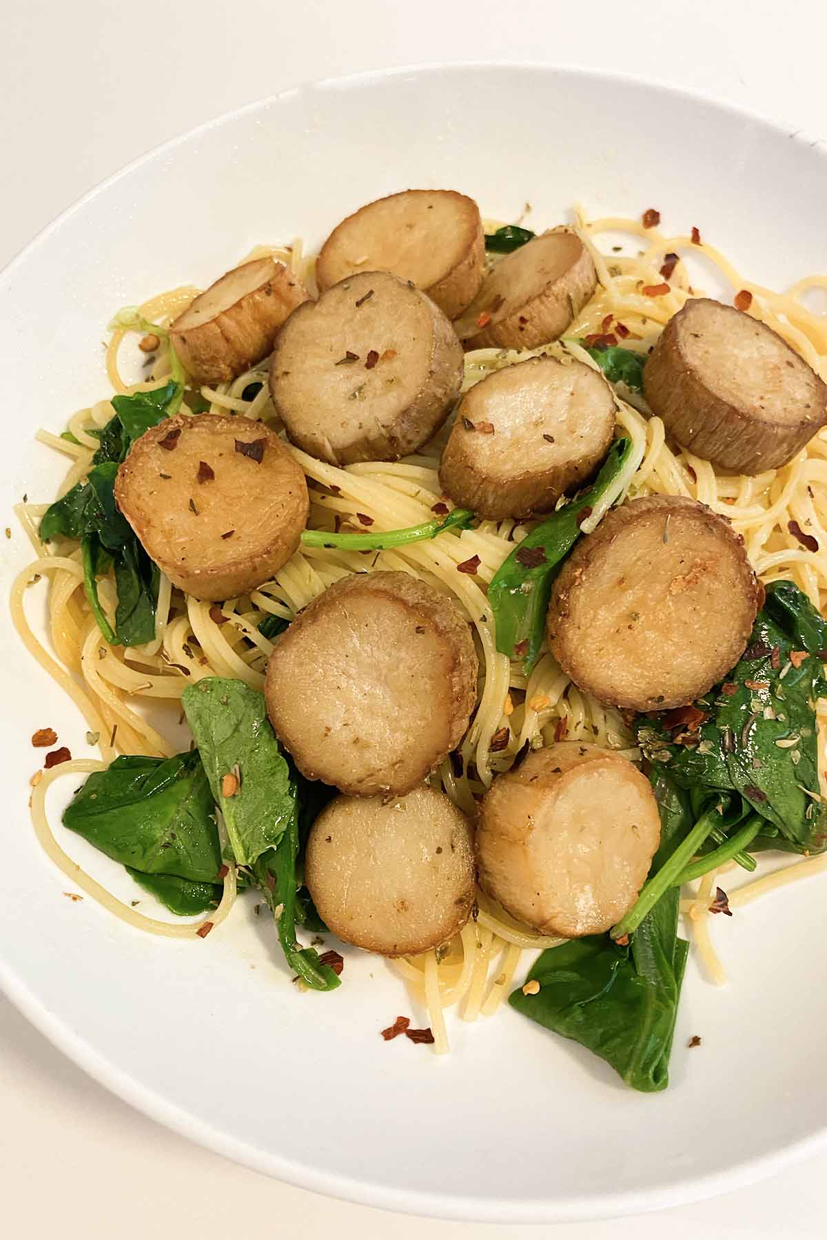 mushroom scallops over spaghetti and spinach in a white bowl