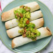 blue plate of air fryer taquitos topped with avocado salad
