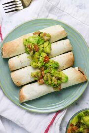 blue plate of air fryer taquitos topped with avocado salad