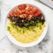 bowl of vegan grits topped with tomato, green onion, and mushroom bacon