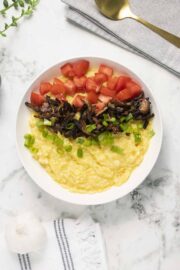 bowl of vegan grits topped with tomato, green onion, and mushroom bacon