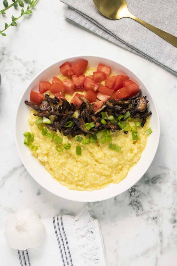 bowl of vegan grits topped with tomato, green onion, and mushroom bacon