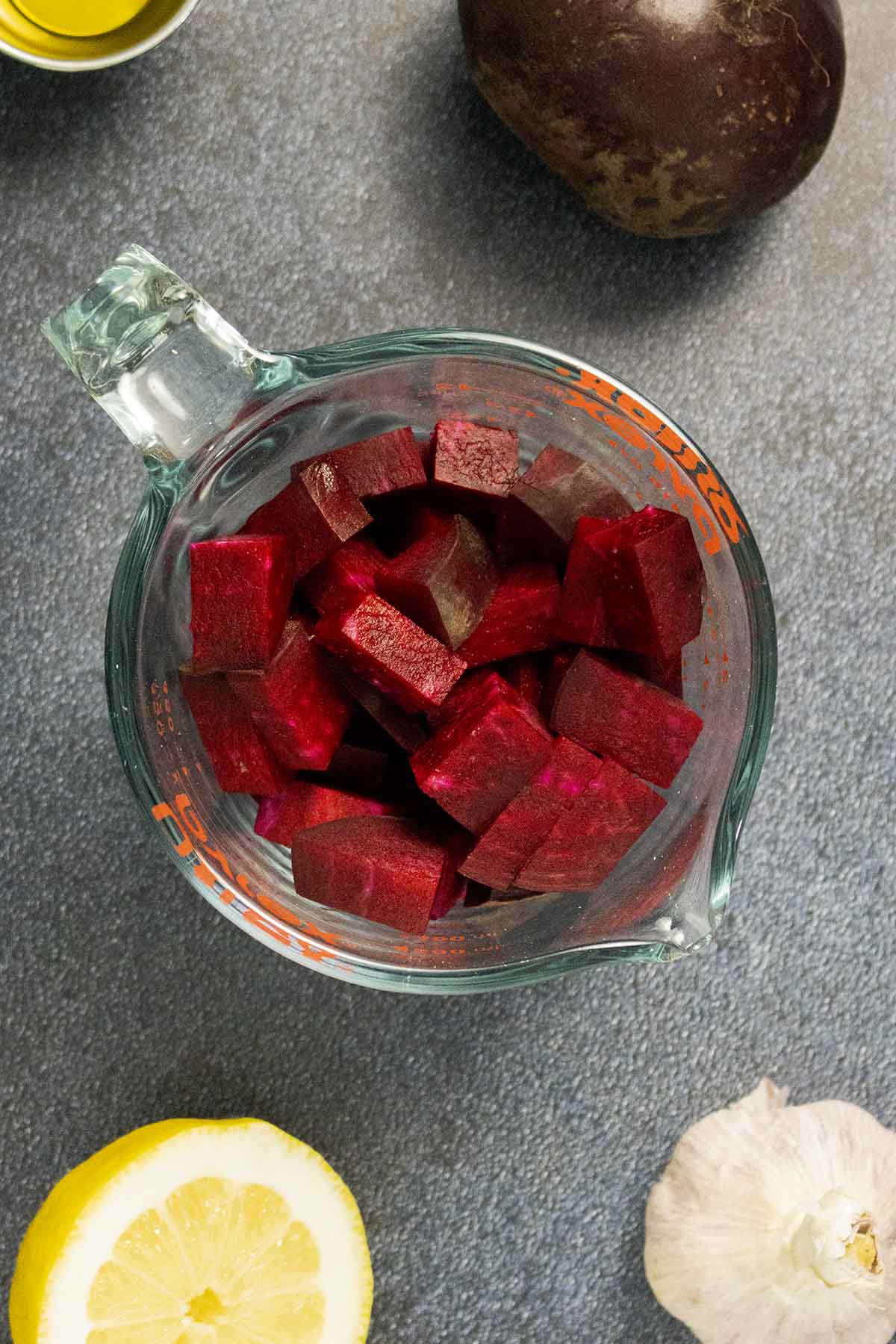 diced beets in a measuring cup with lemon, garlic, and a whole beet on a dark table