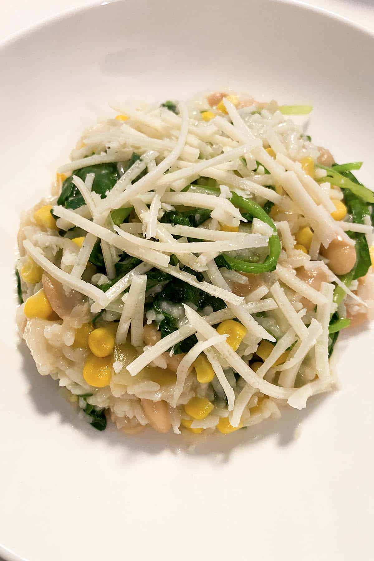 vegan risotto with spinach, onions, and corn on a white plate topped with vegan cheese shreds