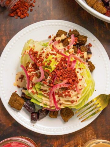 vegan wedge salad with croutons, pickled onions, bacon, and creamy dressing on a white plate
