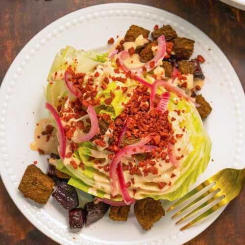 vegan wedge salad with croutons, pickled onions, bacon, and creamy dressing on a white plate