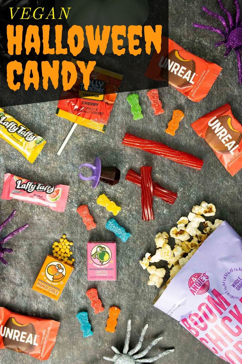 an assortment of vegan Halloween candy on a slate counter with glitter spiders, text overlay