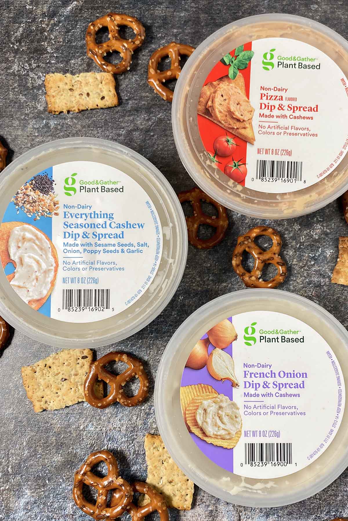 three containers of Good & Gather Plant Based Dip + Spread: pizza, everything bagel, and French onion on a table with pretzels and crackers
