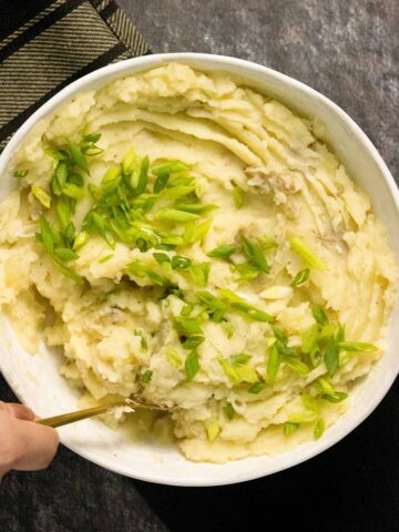 olive oil mashed potatoes in a serving bowl topped with green onion pieces