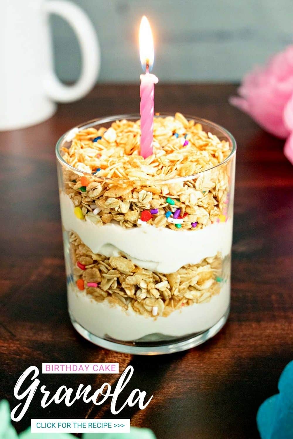 birthday cake granola parfait with yogurt in a glass. It has a candle on top! (text overlay)