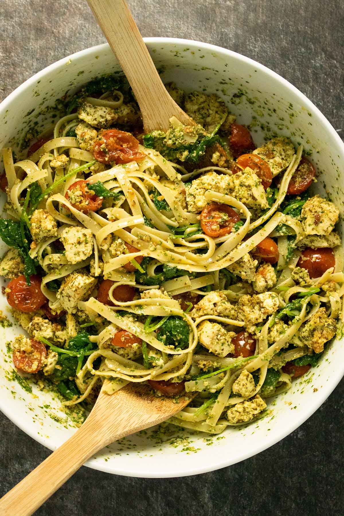 large mixing bowl with pesto tofu pasta and two wooden spoons