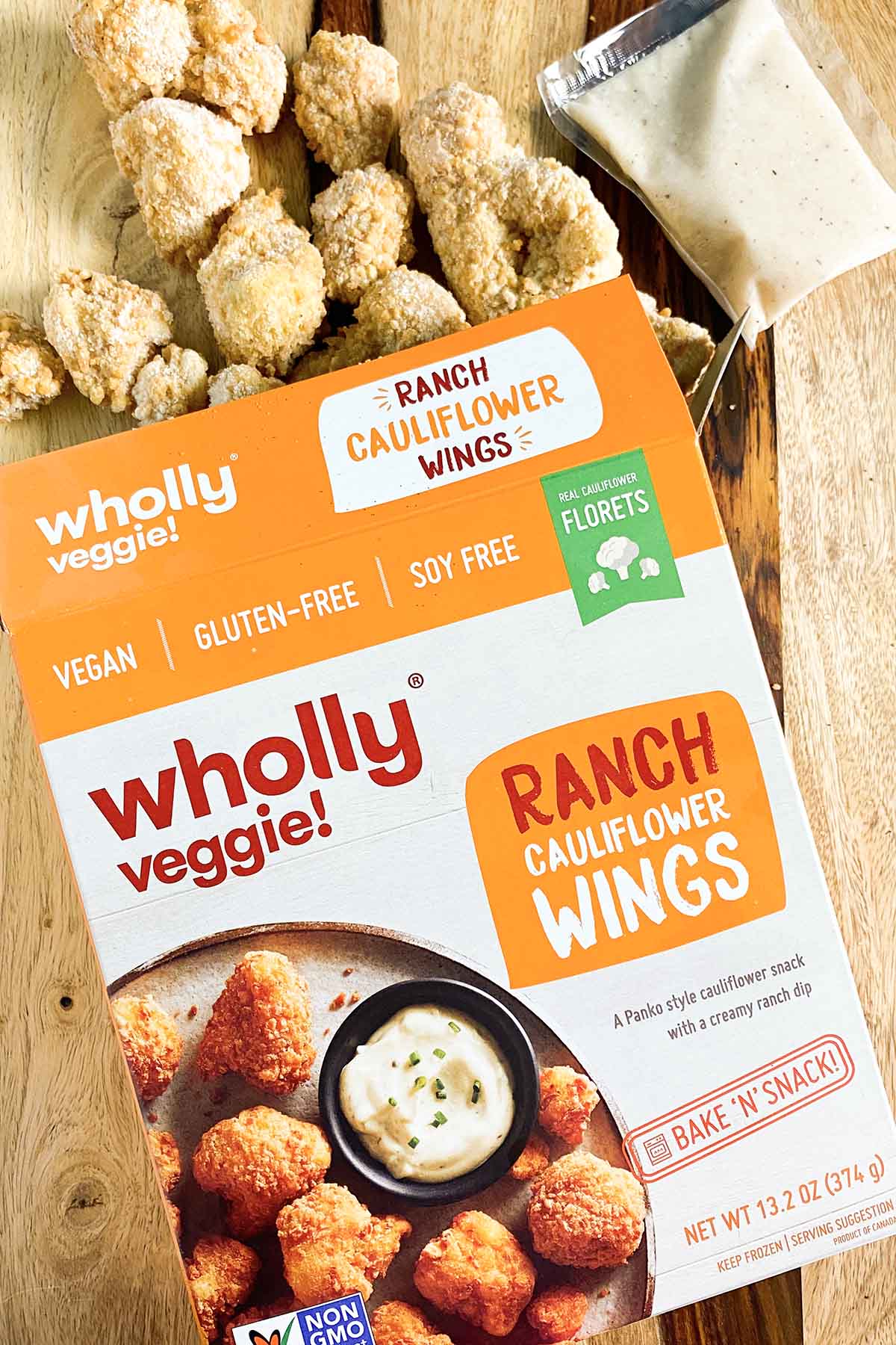 box of Wholly Veggie! Ranch Cauliflower Wings with the frozen wings spilling out onto a wooden table