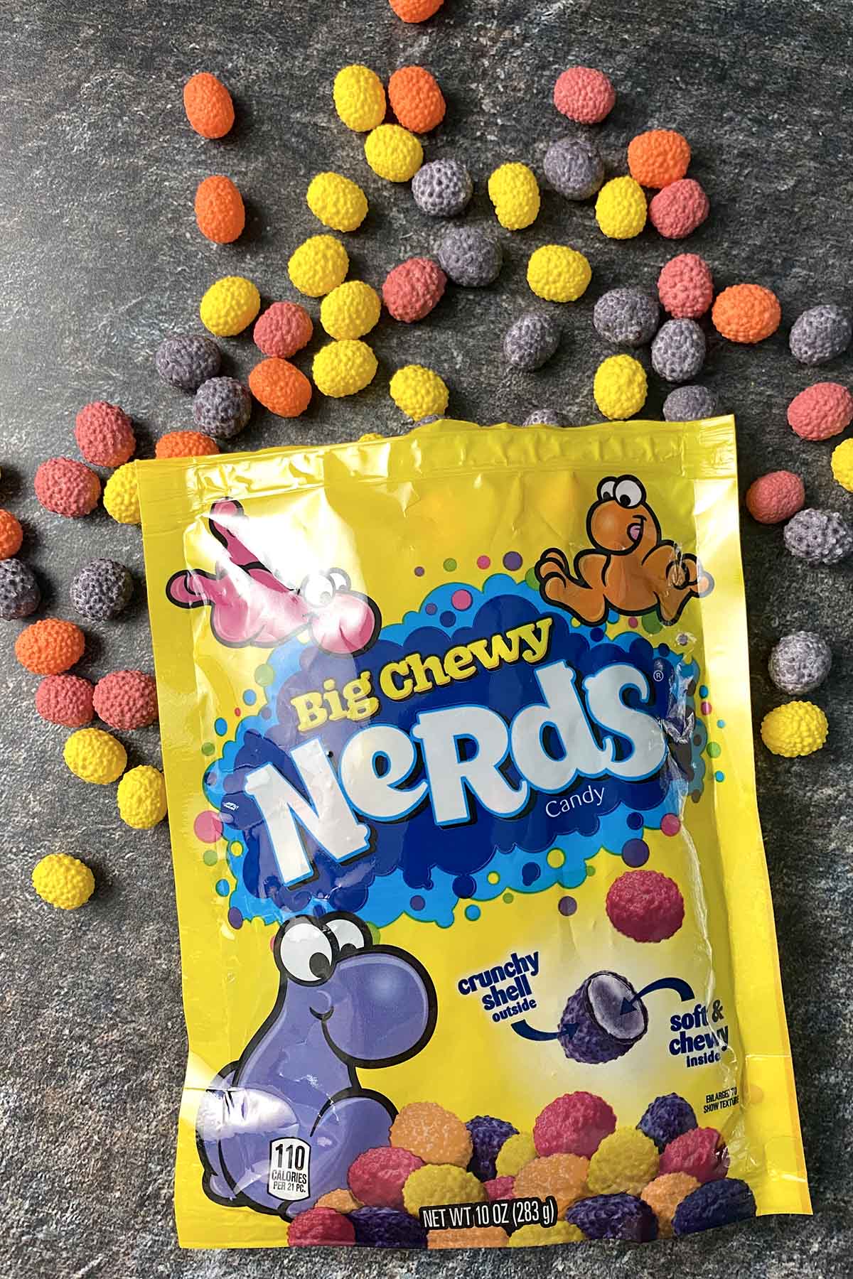 bag of Big Chewy Nerds on a slate table with the pink, purple, yellow, and orange candy all around it