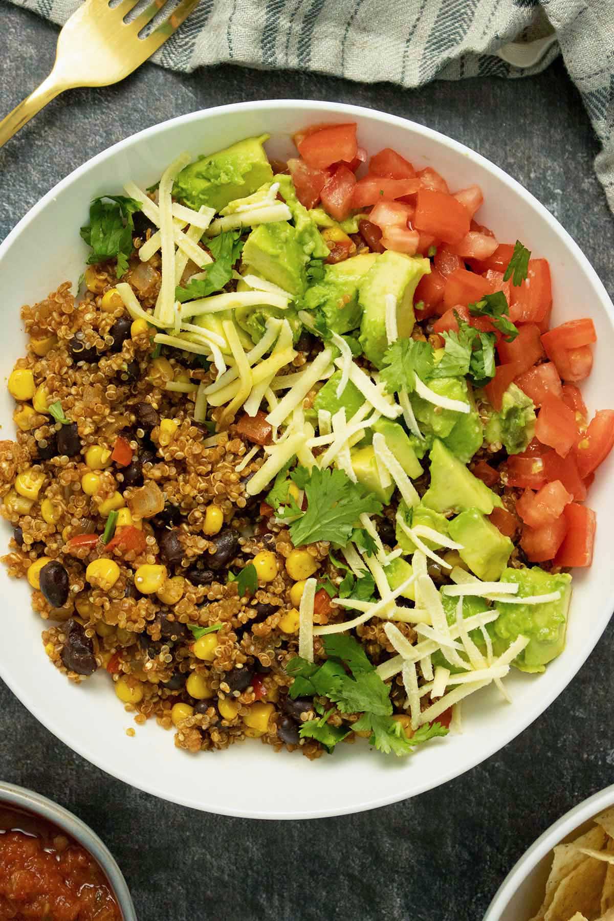 Instant Pot quinoa burrito bowl with beans, corn, and red peppers topped with avocado, tomato, cilantro, and vegan cheese shreds