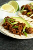 vegan chorizo tacos on a white plate with avocado, green onion, and lime