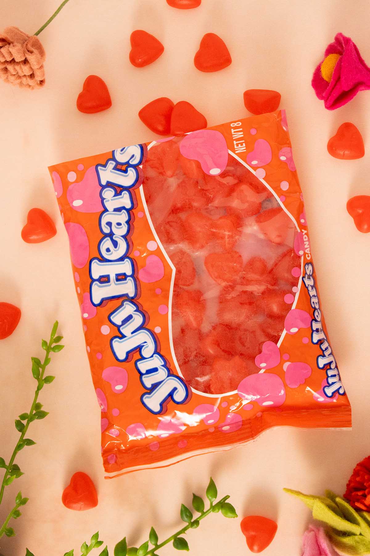 an open bag of JuJu Hearts on a pink table surrounded by flowers and candy hearts