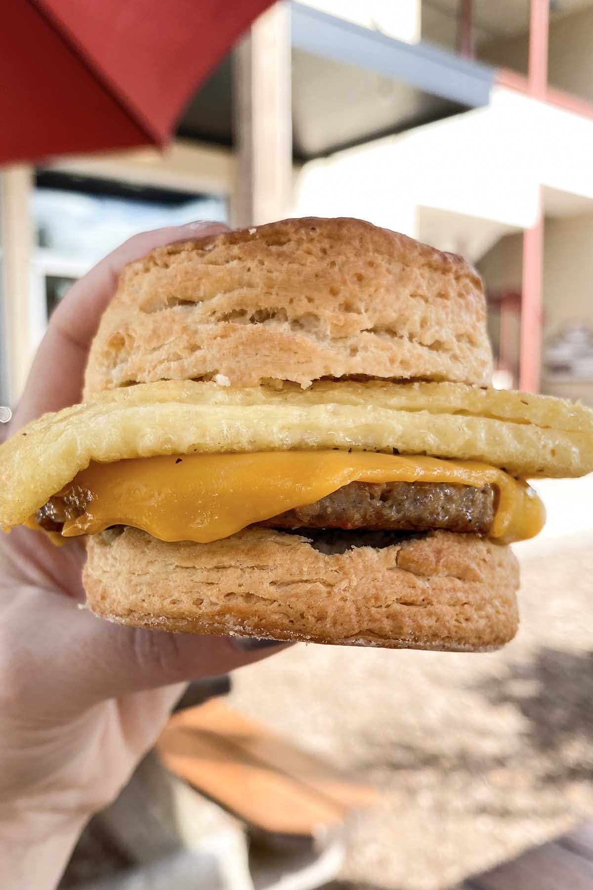 hand holding a biscuit sandwich with vegan sausage, Just egg, and non-dairy cheese