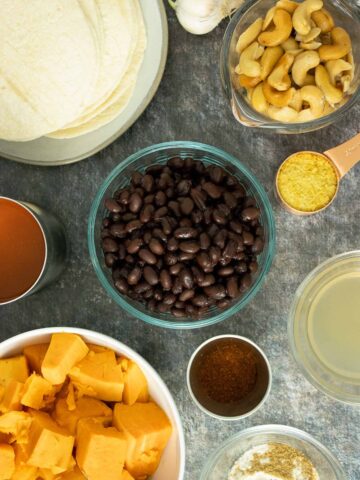 black beans, sweet potatoes, cashews, sauces, and spices in bowls on a slate table
