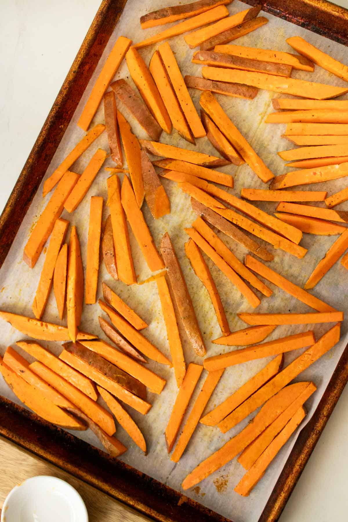 sweet potato fries on the baking sheet after tossing with oil and spices