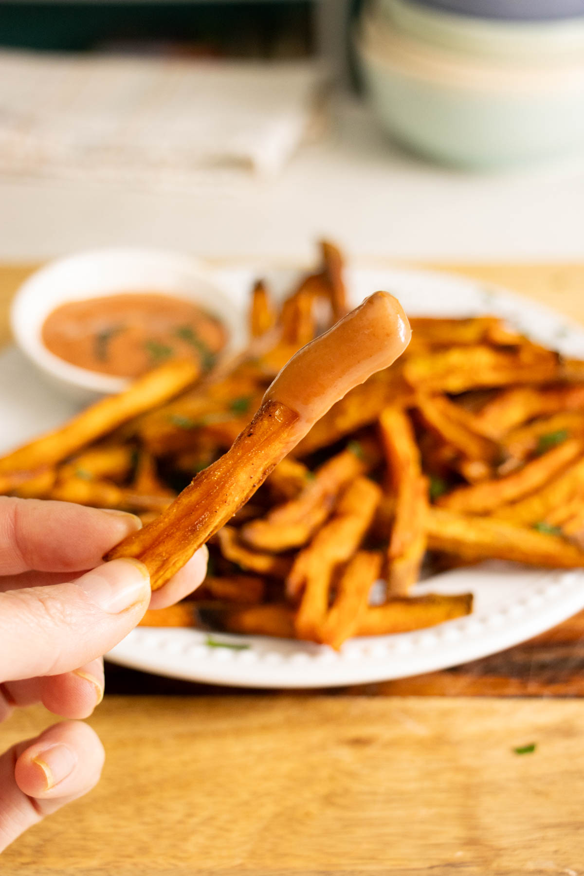 hand holding a curried sweet potato fry dipped in cumin ketchup