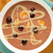 cherry smoothie bowl on a wooden table topped with cherries, orange slices, and tahini